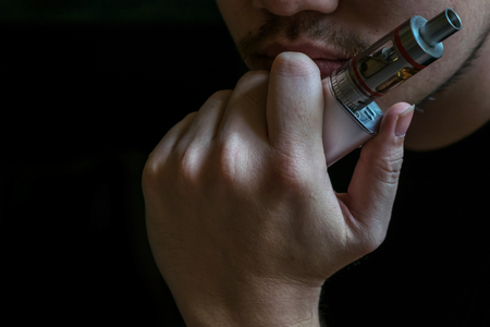 Man with concealed identity smoking a controversial vaping an electronic cigarette. Vaping is debatable in the health community if it is safe or a health riskの写真素材