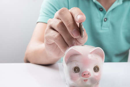 Young businessman depositing money in piggy bank.の写真素材