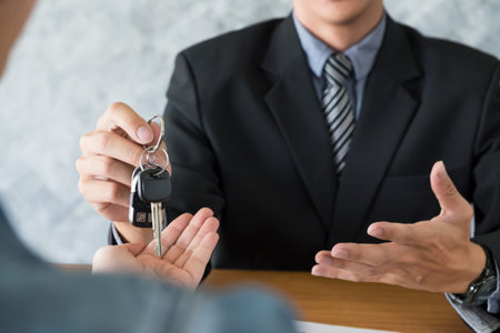 transportation and ownership concept - customer and salesman with car keyの写真素材