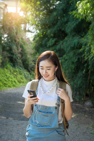 Young asian hipster wear headphone listening to music through smartphone standing outdoors on nature background.の写真素材