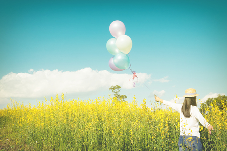 Girl running on the field of yellow flowerwith balloons at sunset. Happy woman on nature, concept about carefree airiness and relax, vintage effect.の写真素材