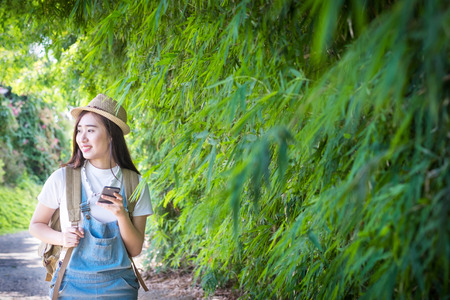 Young asian hipster wear headphone listening to music through smartphone standing outdoors on nature background.の写真素材