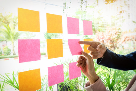 Close up shot of hands of woman sticking adhesive notes on glass wall in office