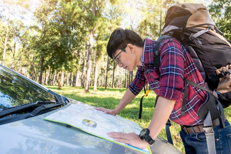 Hands closeup of a young traveler man looking at a map on car trunk.