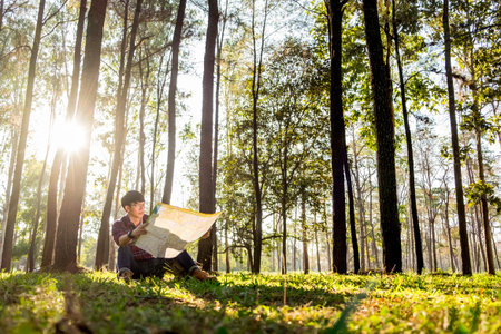 Traveler man hiker walking under the rays of the sun in the mountain forest and watching map.の写真素材