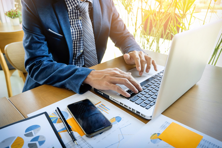 Business man working at office with laptop, tablet and graph data documents on his deskの写真素材
