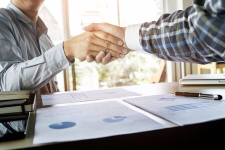 Two confident businessmen handshaking and smiling while sitting at the table together.の写真素材
