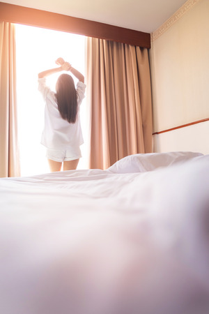 Healthy Woman stretching in bed room and open the curtains after wake up, back view, lifestyle people in cozy indoor comfortable relaxing space.の写真素材