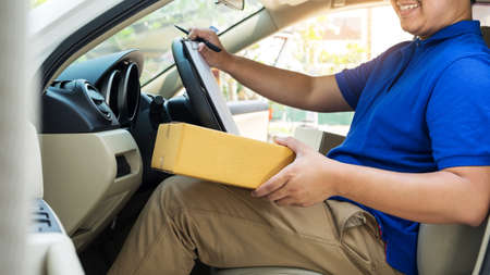 Delivery man with cardboard box checking document list In van and parcels on seat outside the warehouse.の写真素材