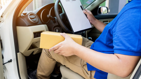 Delivery man with cardboard box checking document list In van and parcels on seat outside the warehouse.の写真素材