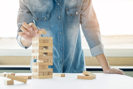 Hand of engineer playing a blocks wood tower game (jenga) on blueprint or architectural projectの写真素材