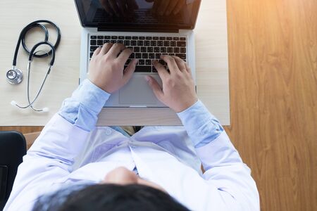Close up of unknown male doctor sitting at the table near the window in hospital and typing at laptop computer..の写真素材