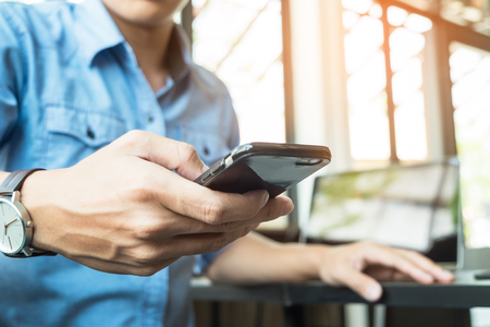 Smiling young casual business man with mobile phone in the hand in office.の写真素材