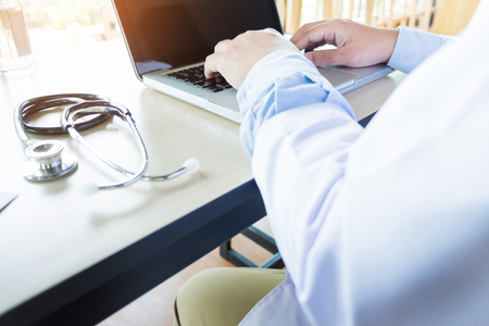 Close up of unknown male doctor sitting at the table near the window in hospital and typing at laptop computer..の写真素材