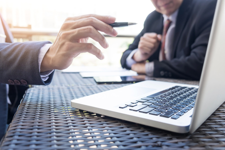 Two businessmen discussing planing tasks with laptop computer sitting at outdoor table.の写真素材