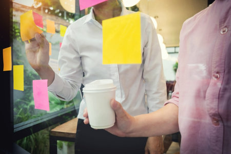 business man sticking adhesive notes on glass wall in office and discussting with team.