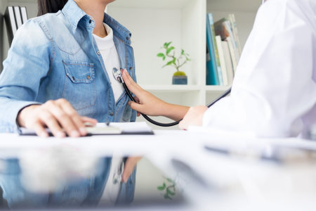 Doctor listening to cheerful young patients chest with stethoscope in his office at the hospital.の写真素材