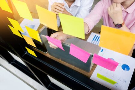 business man sticking adhesive notes on glass wall in office and discussting with team.の写真素材