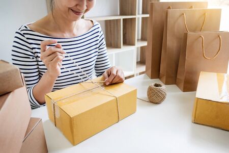 Business owner woman working online shopping prepare product packaging process at her home, young entrepreneur conceptの写真素材