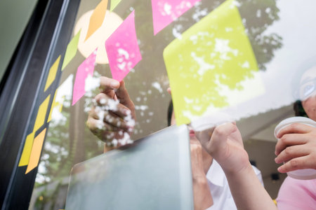 business man sticking adhesive notes on glass wall in office and discussting with team.