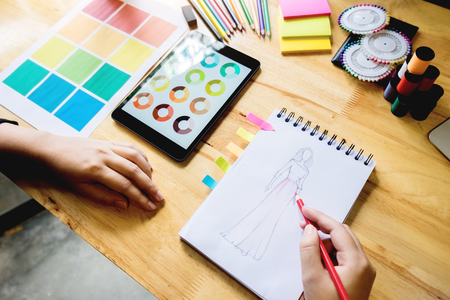 young women working as fashion designer drawing sketches for clothes in atelier paper at workplace studioの写真素材