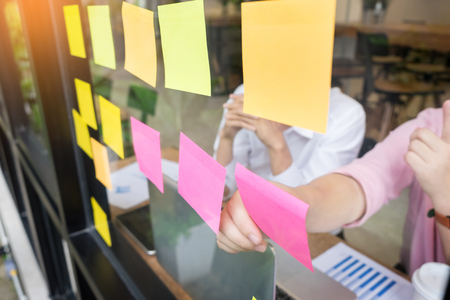 business man sticking adhesive notes on glass wall in office and discussting with team.の写真素材