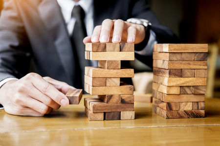 Planning, risk and wealth strategy in business concept, businessman and insurance gambling placing wooden block on a tower.の写真素材
