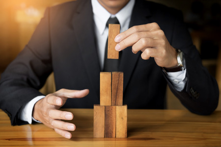 Planning, risk and wealth strategy in business concept, businessman and insurance gambling placing wooden block on a tower.の写真素材