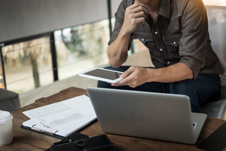 Modern businessman with tablet computer reading news and work report document at morning in cafe.の写真素材