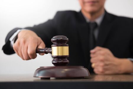 Male Judge lawyer In A Courtroom Striking The Gavel on sounding block in his office.の写真素材