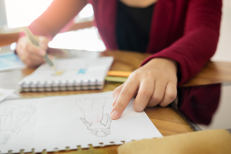 young women working as fashion designer drawing sketches for clothes in atelier paper at workplace studioの写真素材