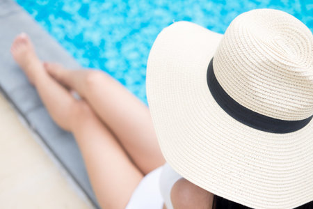 Unrecognizable woman in big hat enjoying relaxing on the swimming pool at luxury villa, travel near the sea and beach in the sunset.の写真素材