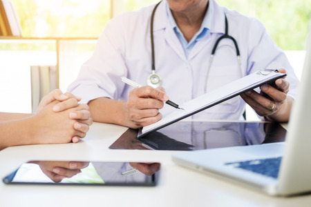 patient listening intently to a male doctor explaining patient symptoms or asking a question as they discuss paperwork together in a consultationの写真素材