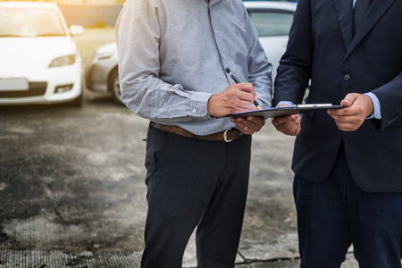 Car insurance agent send a pen to his customers sign the insurance form on clipboard while examining car after accident claim.の写真素材