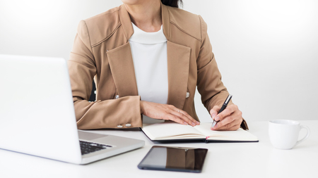 Attractive women in casual business sitting at a table working on her laptop computer at home office in front of a windowの写真素材