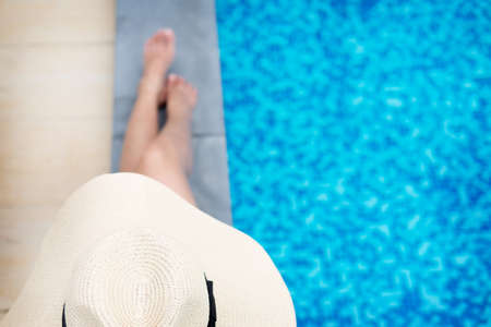 Unrecognizable woman in big hat enjoying relaxing on the swimming pool at luxury villa, travel near the sea and beach in the sunset.の写真素材