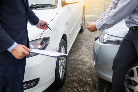 Insurance agent writing on clipboard while examining car after accident claim being assessed and processedの写真素材