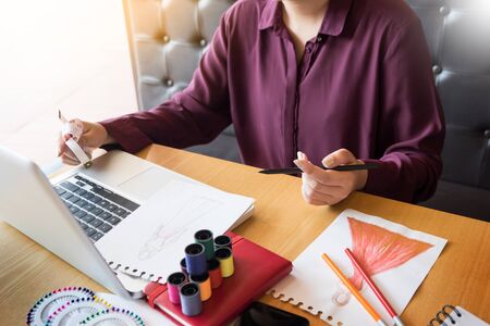 young women working as fashion designer drawing sketches for clothes in atelier paper at workplace studioの写真素材