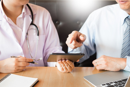 Two doctors discussing patient notes in an office pointing to tablet as they make a diagnosis or decide on treatment.の写真素材