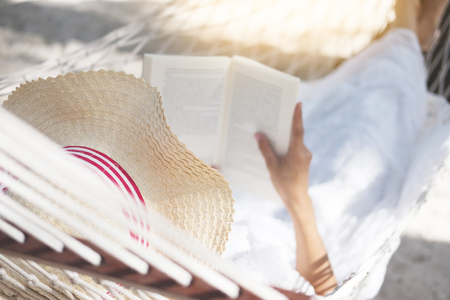 Young lady reading a book in hammock on tropical sandy beachの写真素材