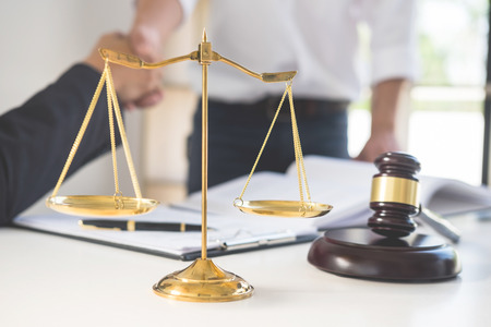 Gavel Justice hammer on wooden table with judge and client shaking hands after adviced in background at courtroom, lawyer service conceptの写真素材