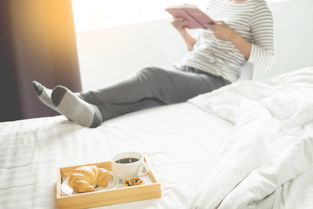 Woman reading book or newspaper and drinking coffee breakfast on bed during the morning.の写真素材