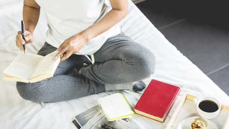Young woman sitting working and writing in the notebook on bed leisure concept taking notes, Comfortable female workplace. Memories, planning , educationの写真素材