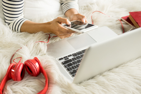 A beautiful caucasian woman lying down on the bed pretty girl using cellphone and using a laptop notebook on bed, resting.の写真素材