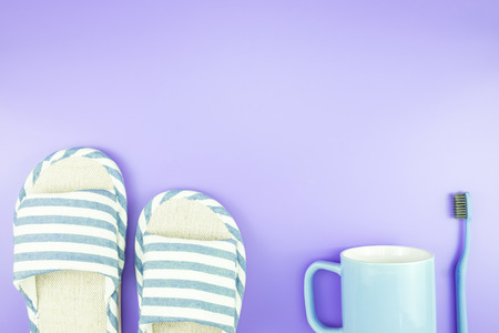 home equipment clock flat lay composition tooth brush glasses, towel and slippers top view on blue and purple violet conceptの写真素材