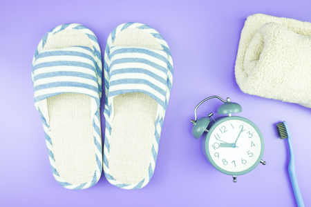 home equipment clock flat lay composition tooth brush glasses, towel and slippers top view on blue and purple violet conceptの写真素材