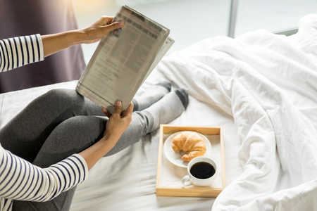 Woman reading book or newspaper and drinking coffee breakfast on bed during the morning.の写真素材