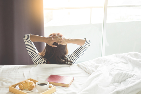 Attractive asian woman stretch oneself awaking on the bed roomの写真素材
