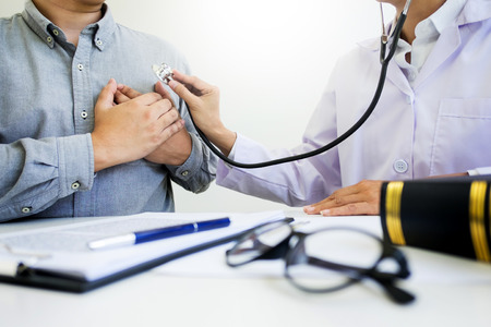 Male Patient Visiting Doctor's Office listening to checking patients chest with stethoscope in medical officeの写真素材