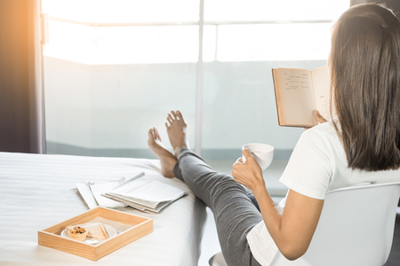 Woman reading book or newspaper and drinking coffee breakfast on bed during the morningの写真素材